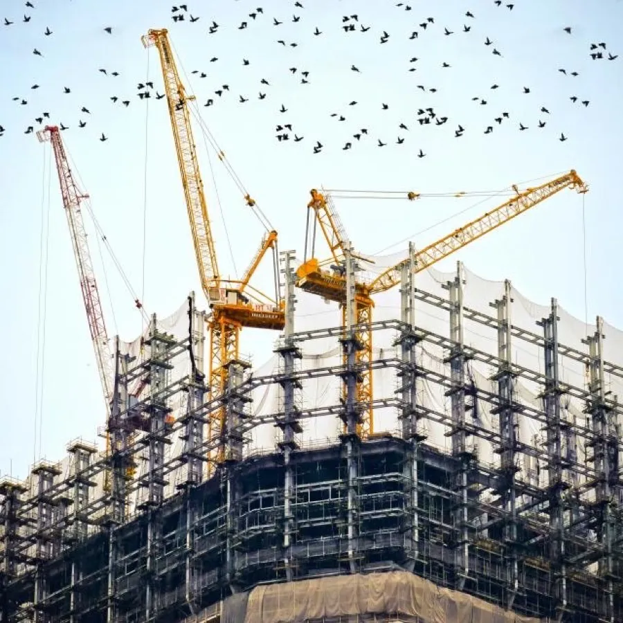 A high-rise structure under construction, framed by tower cranes against the sky.